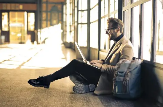 Man sitting by a window at a Budapest train station, working on his laptop with sunlight streaming through.